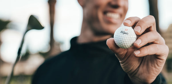 En person håller upp en Hitpin golfboll med siffran 59 på